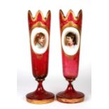A pair of Bohemian cranberry glass and gilt vases, each with an oval enamelled panel depicting a