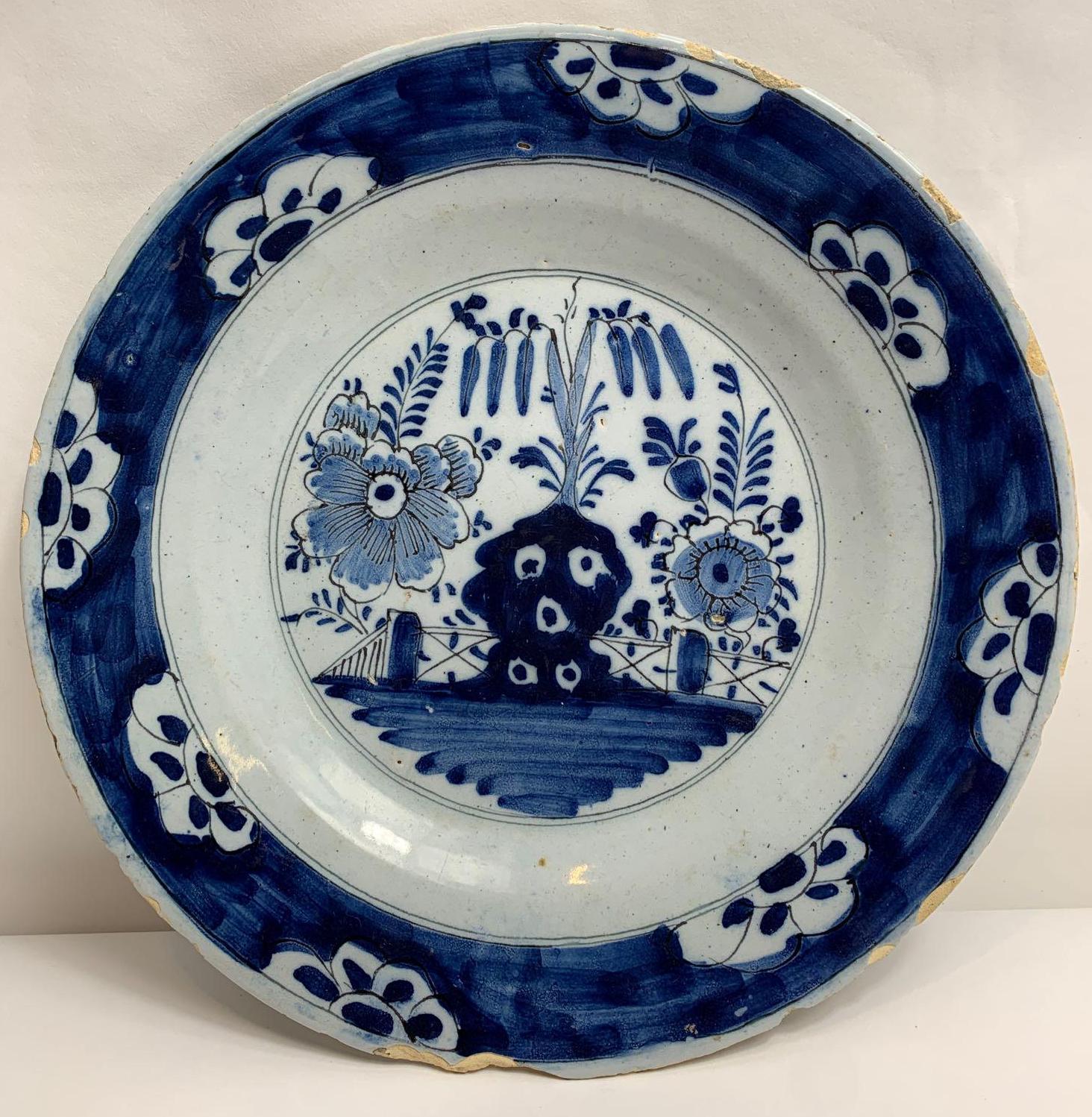 A blue and white Delft plate, decorated with plants and flowers, 23.5cm diameter