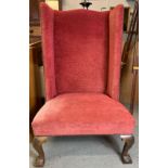 A high sided wingback armchair on ball and claw feet, upholstered in red velvet type fabric