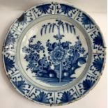 A large blue and white Dutch Delft charger, decorated with a central panel of flowers and a repeated