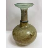 A Roman glass bottle, standing on a concave base with a green ring around the neck, probably 1st-2nd