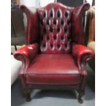 A wing back red leather armchair of curved form, with button back and nail head decoration to the