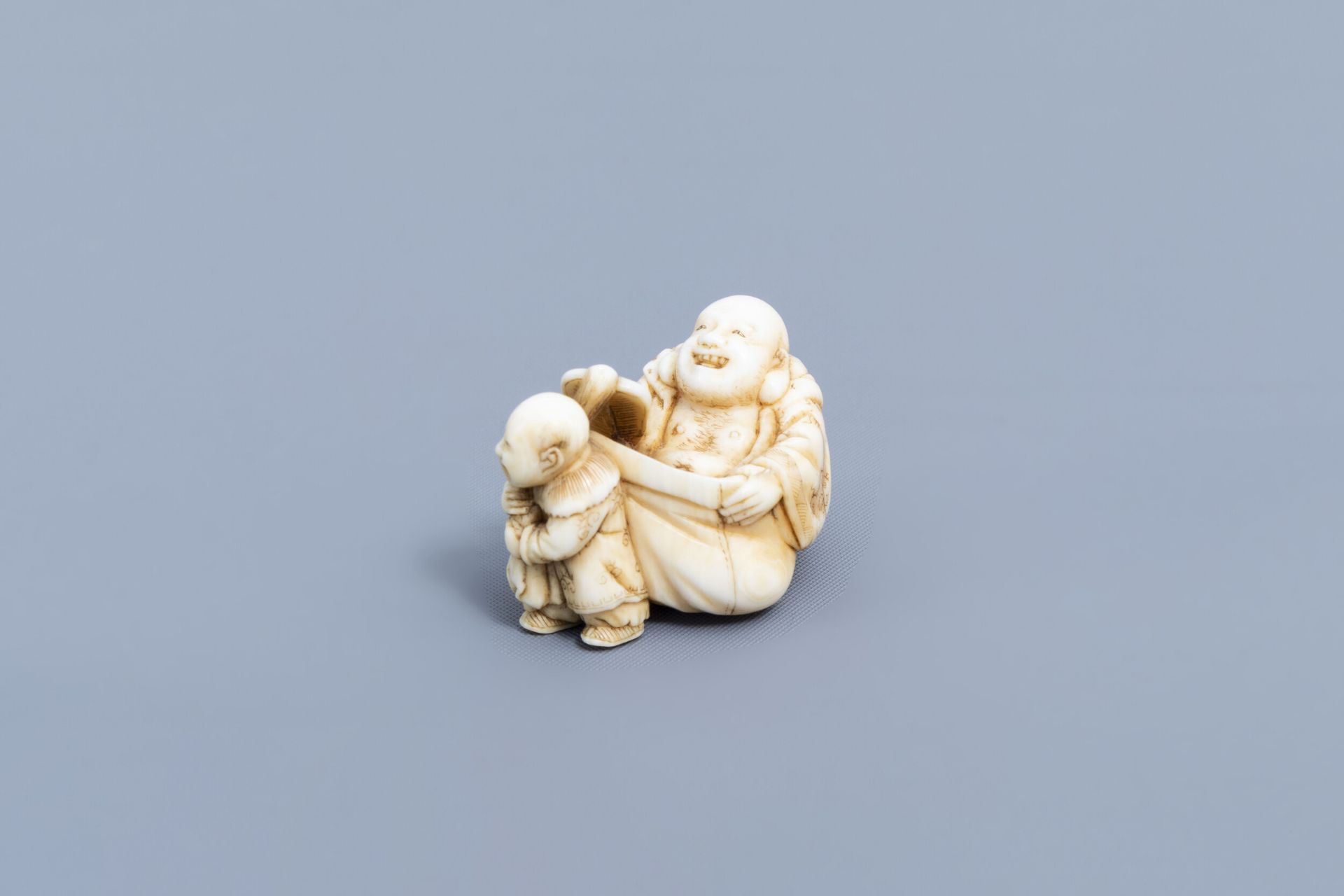 A Japanese ivory netsuke of a laughing Buddha with his servant, signed Shinsai, Edo