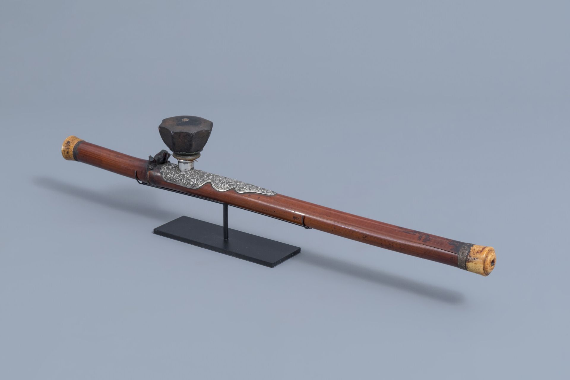 A Chinese bamboo opium pipe with a silver saddle, ivory endpiece and stoneware damper, 19th C.