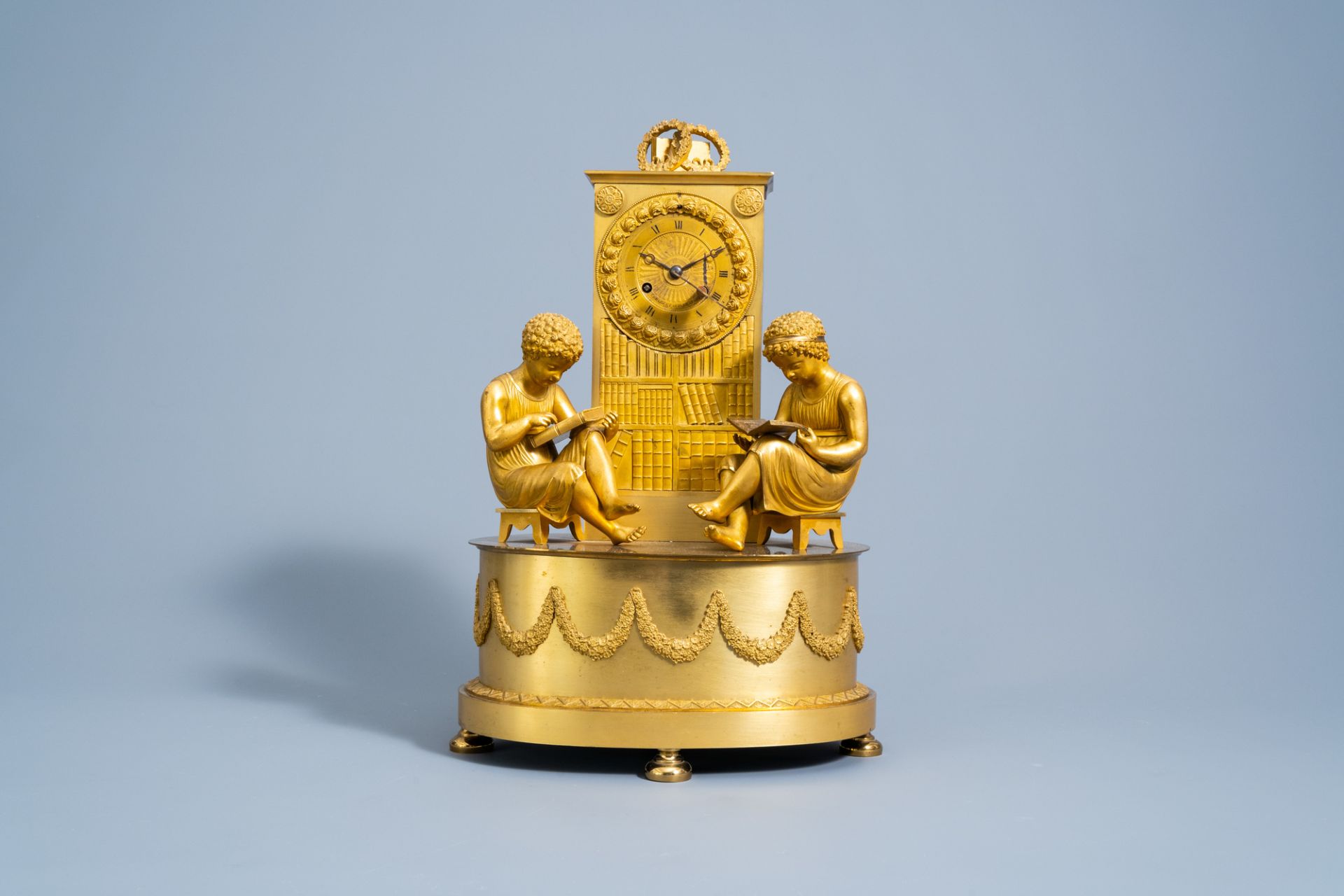 A fine French Empire gilt bronze mantel clock with children reading in a library, 19th C.