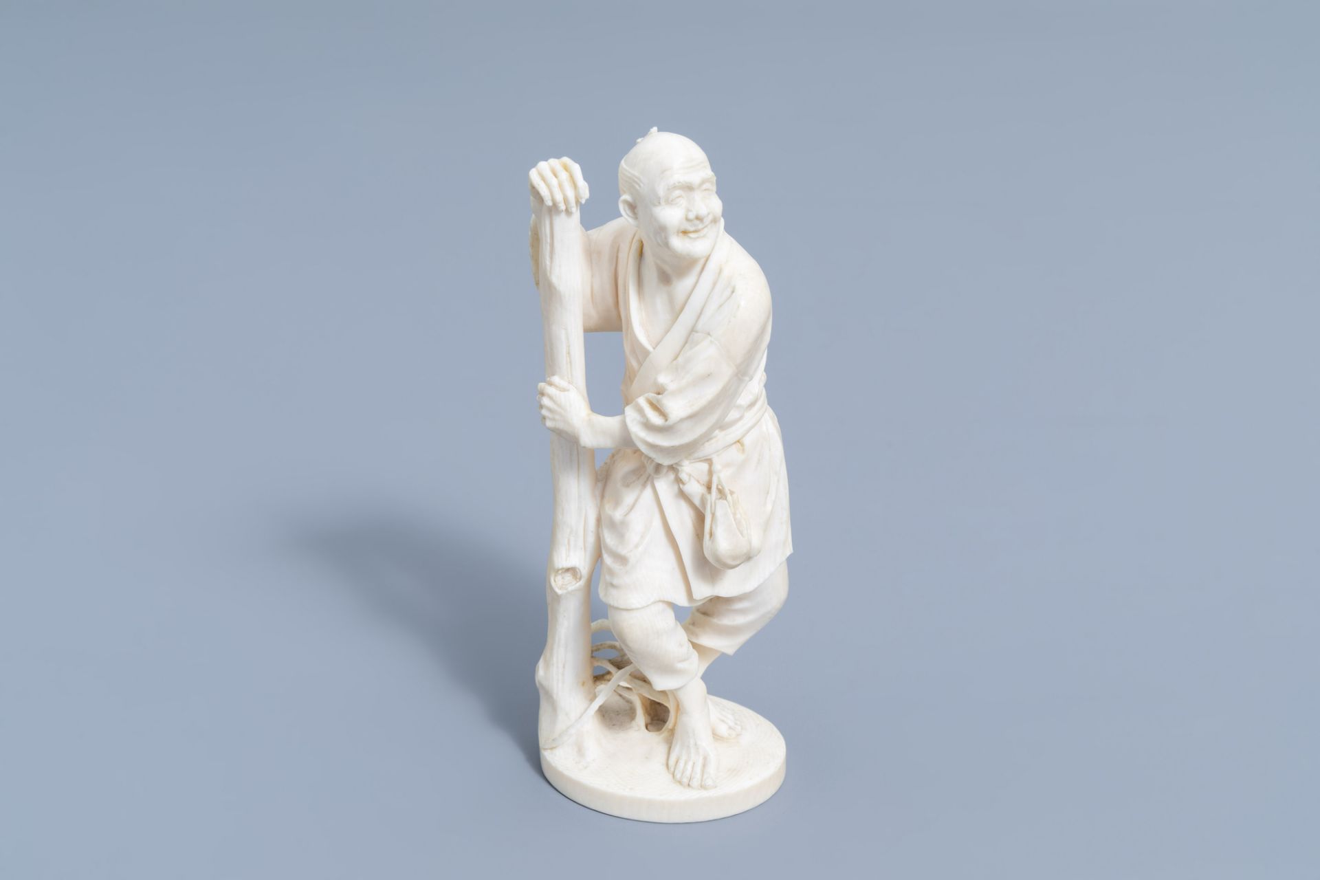 A Japanese ivory okimono of a farmer leaning against a tree, signed Kogyoku, Meiji, early 20th C.