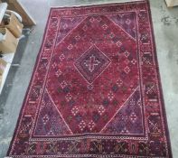 Red ground rug with central diamond-shaped medallion, allover hook-shaped motifs in reds, blues