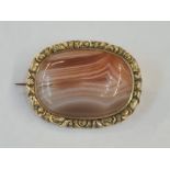 Early Victorian gilt metal brooch set with a central cabochon agate within a chased floral border,