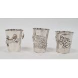 Three Chinese silver-coloured shot cups, each variously decorated with dragons or lizard and spider,