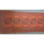 Modern Eastern-style red ground runner with repeating central medallions in reds and blacks, 387cm x