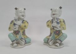 Pair of Chinese porcelain seated figures, laughing boys, each holding a blue and white vase, 16cm