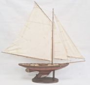 Varnished wood model yacht with canvas sails and metal fittings and the associated wooden stand,