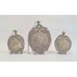 Three silver coloured metal gunpowder flasks, possibly Russian, all relief decorated, two