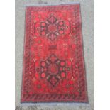 Modern Eastern-style red ground rug with two central medallions, in reds and blacks, 128cm x 76cm