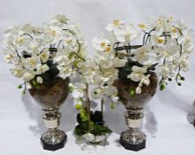 Two large silver coloured metal and glass vases with faux orchids displayed, and a glass bowl of