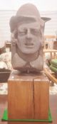 Stone bust carving of a man wearing a hat with collar visible, on square wooden base, 65cm high