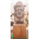 Stone bust carving of a man wearing a hat with collar visible, on square wooden base, 65cm high