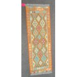 Chobi kilim runner with lozenges of green and blue on an orange ground, 200cm x 66cm.