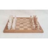 Modern carved stone chess set on wooden board, 40cm wide