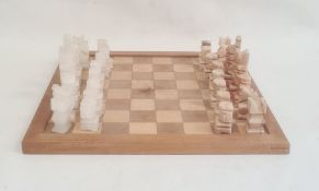 Modern carved stone chess set on wooden board, 40cm wide