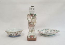 Porcelain standing figure of a man holding a vase containing a lotus flower, 27cm high on wooden