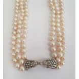 Diamond and pearl triple strand necklace having diamond set bow-shaped clasp with collet set stone