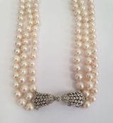 Diamond and pearl triple strand necklace having diamond set bow-shaped clasp with collet set stone