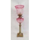 Cranberry and brass oil lamp having panelled flared shade, cranberry well, on reeded column,