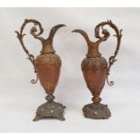 Pair of ornate metal ewers, the copper bodies with gilded mounts, with scroll handles, on circular