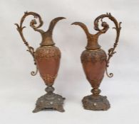 Pair of ornate metal ewers, the copper bodies with gilded mounts, with scroll handles, on circular