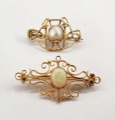 Gold-coloured brooch set with central oval opal cabochon within a scrolling wirework frame,