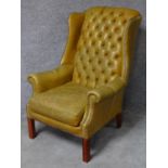 A Georgian style leather upholstered button back wing armchair on square mahogany supports. H.100cm
