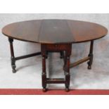 An antique country oak drop flap dining table with frieze drawer and gateleg action on turned