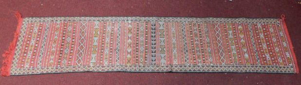 A Kilim style runner with repeating geometric design on red ground, fringed 290x65cm