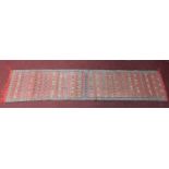 A Kilim style runner with repeating geometric design on red ground, fringed 290x65cm