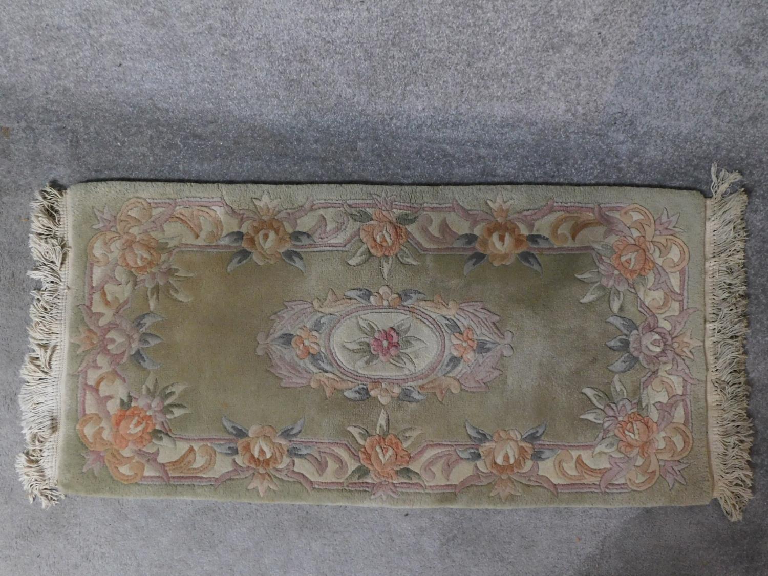 A Chinese rug with central floral medallion set on a pastel field within floral borders 144x63cm