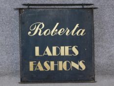 A vintage wall mounted hanging iron sign written 'Roberta ladies fashions'. 60x71cm