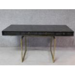 A contemporary designer writing table with ebonised top and four drawers on heavy brass pedestal