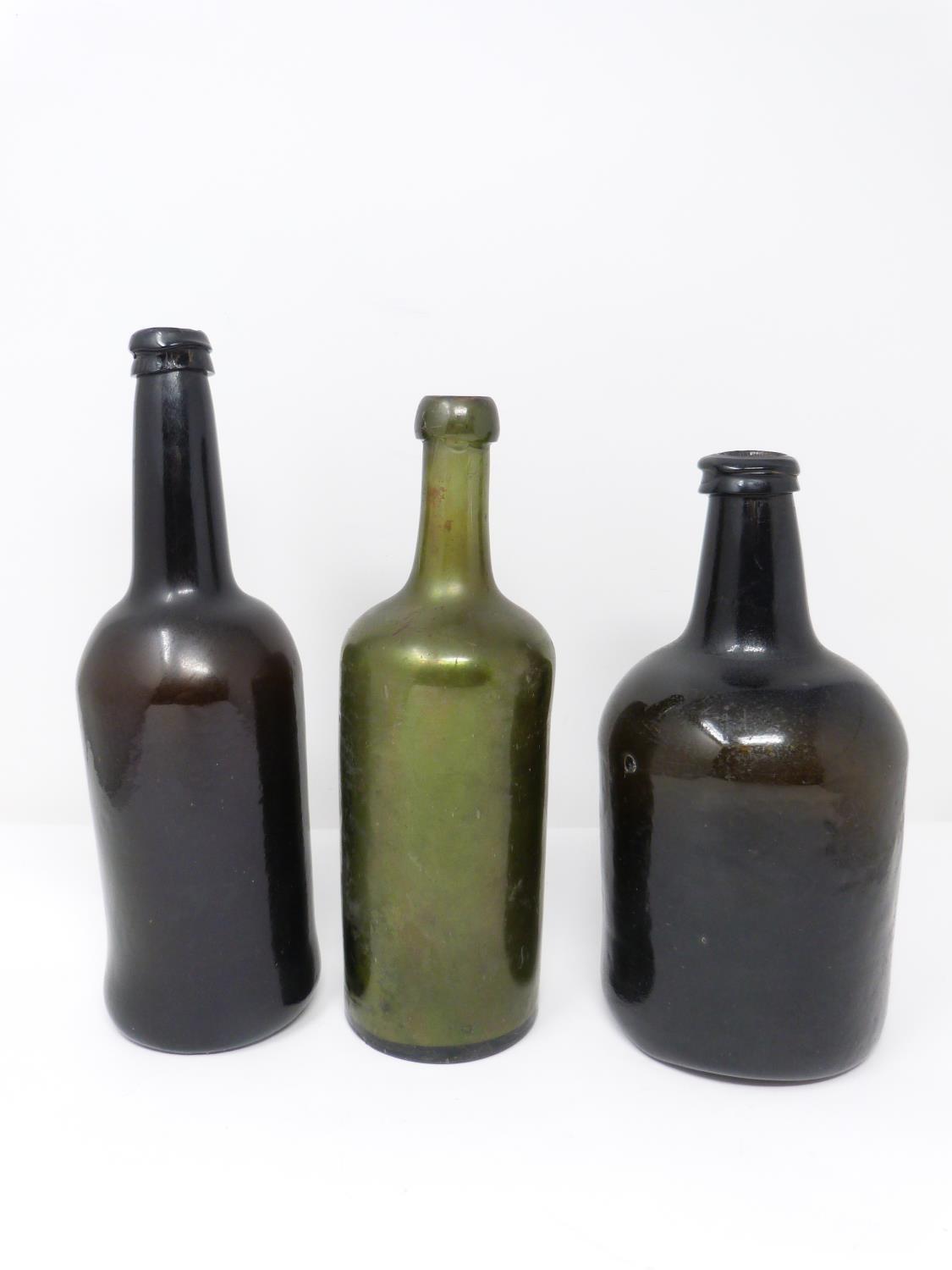 Three 18th century glass wine bottles. Two brown mallet shaped bottles and one green cylindrical