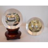 A pair of reverse painted glass spheres, one mounted on a wooden stand, one depicting a landscape