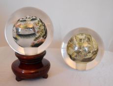 A pair of reverse painted glass spheres, one mounted on a wooden stand, one depicting a landscape