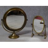 Two Edwardian brass framed swing toilet mirrors. One oval on a four footed linear stand the other