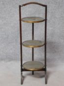 A late 19th century mahogany three tier folding cake stand fitted with embossed brass trays. maker's