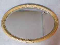 An oval gilt framed wall mirror with reeded and ribbon decoration fitted with bevelled plate.