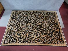 A Chinese woollen rug with repeating floral motifs on an ebony field within floral borders, fringed.