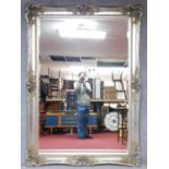 A large decorative wall mirror in silvered Rococo scrolling frame inset with bevelled plate.