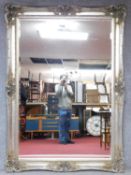 A large decorative wall mirror in silvered Rococo scrolling frame inset with bevelled plate.