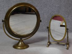 Two Edwardian brass framed swing toilet mirrors. One oval on a four footed linear stand the other