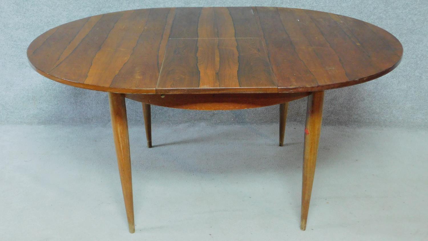 A vintage rosewood extending dining table on circular tapering supports fitted with swivelling