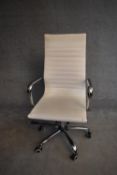 A Charles Eames style swivel office armchair in cream vinyl upholstery. H.110x56cm